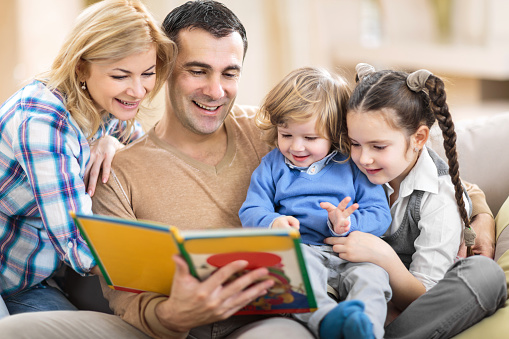 Smiling parents reading a book to their little children.