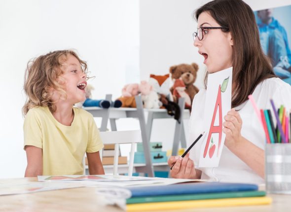 A happy child pronouncing a letter during speech therapy with a specialist.
